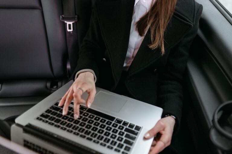 Persoană care analizează pe laptop anunțuri cu mașini second-hand, cu un carnet de notițe alături